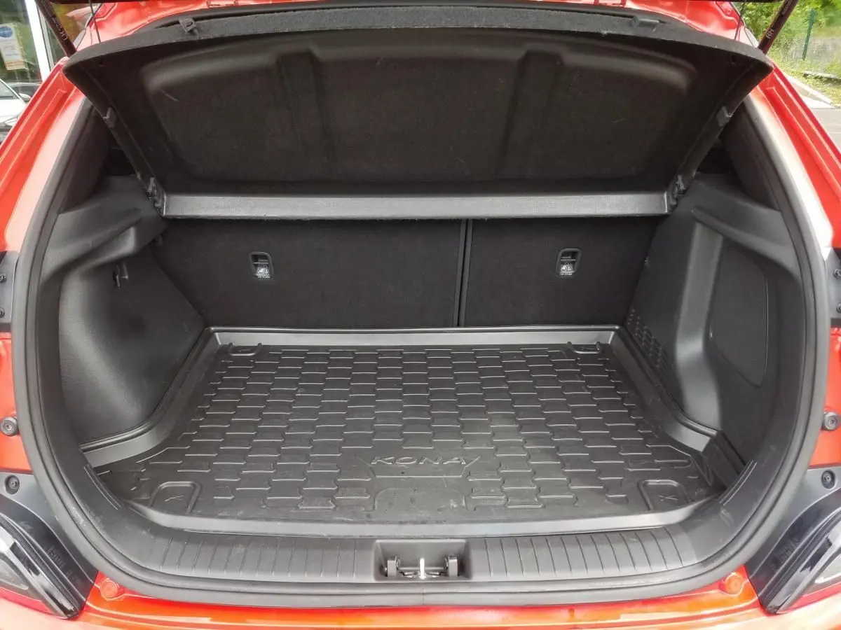 Coffre ouvert vu de l'arrière d'un Hyundai Kona rouge avec tapis de coffre noir marqué Kona.