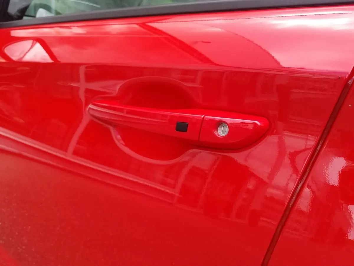 Poignée de porte côté gauche rouge vif d'une Hyundai Kona 2023, finition N Line avec serrure et bouton noir intégré.