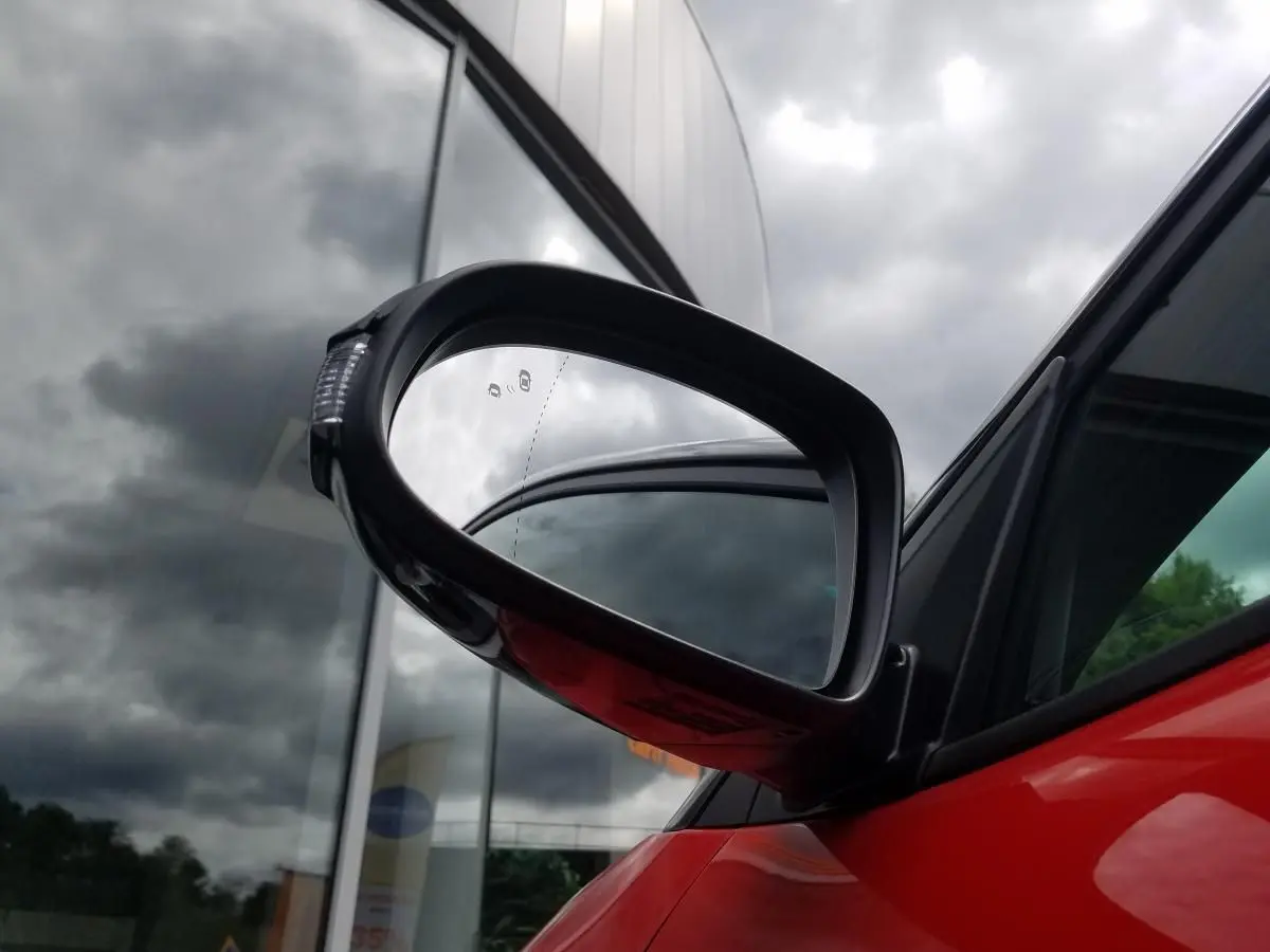 Rétroviseur extérieur droit noir contrasté du Hyundai Kona rouge, avec vitre arrière surteintée visible en arrière-plan.