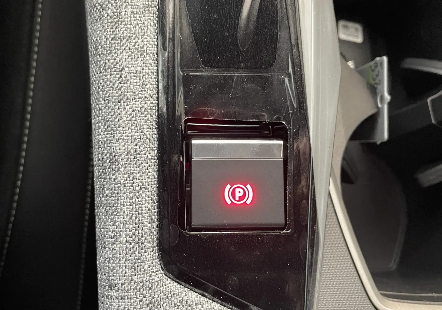 Gros plan sur le bouton de frein à main électrique rouge dans la console centrale du Peugeot 3008 Hybrid noir.