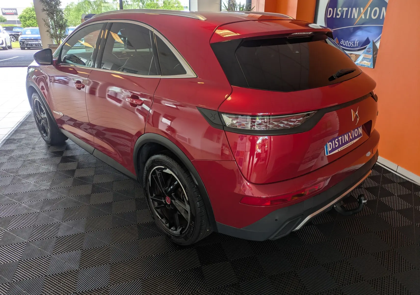 Vue 3/4 arrière droite d’un DS7 rouge 2019 avec attelage et jantes noires, stationné en intérieur sur sol noir.