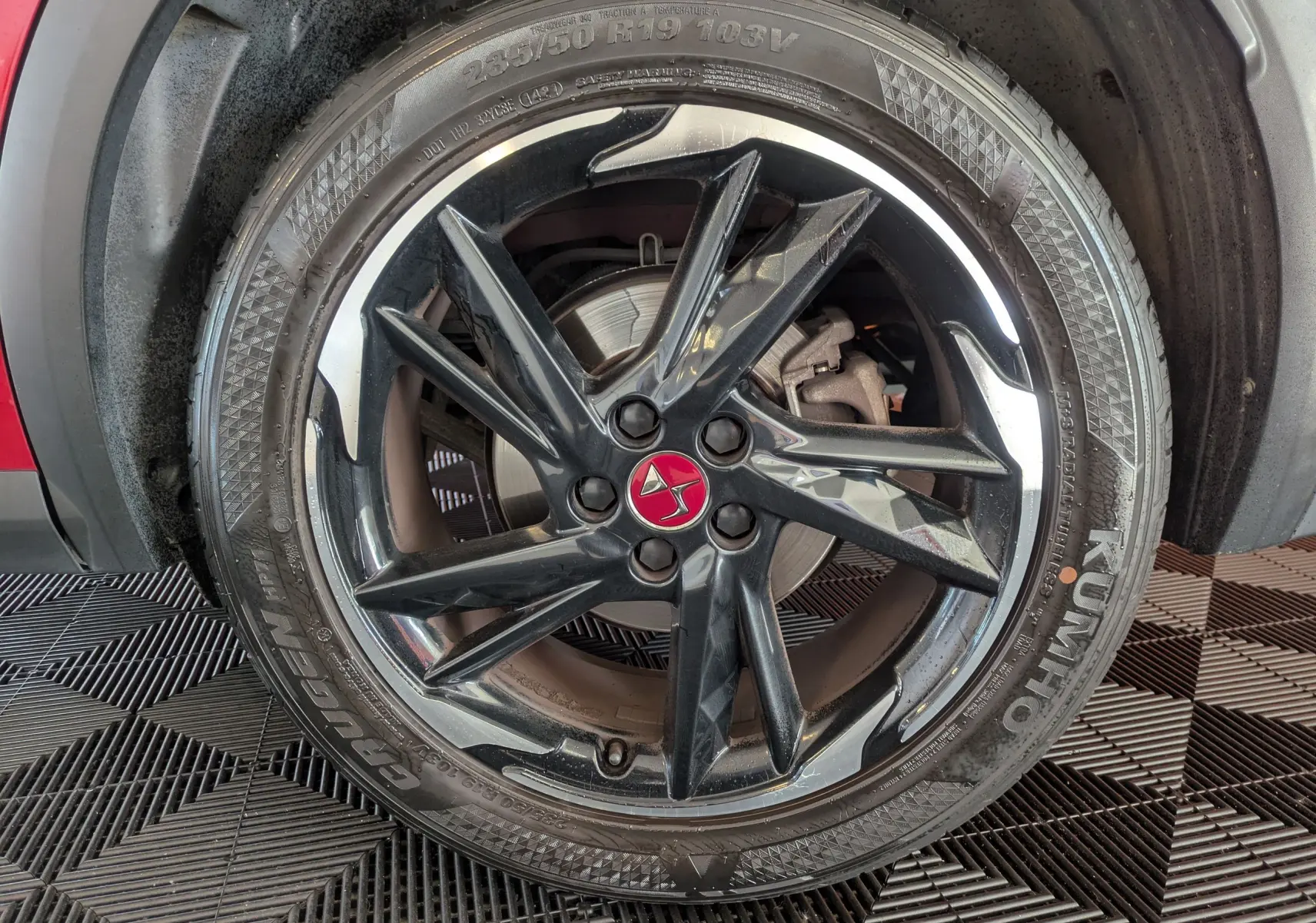 Gros plan sur la roue avant gauche du DS7 rouge 2019, jante noire brillante avec logo DS rouge au centre.