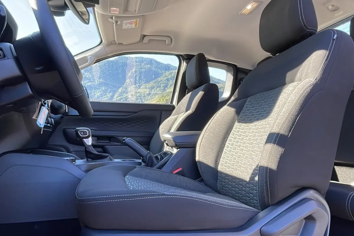 Vue intérieure côté conducteur du Ford Ranger 2025, sièges tissu gris avec accoudoir central et volant cuir multifonctions.