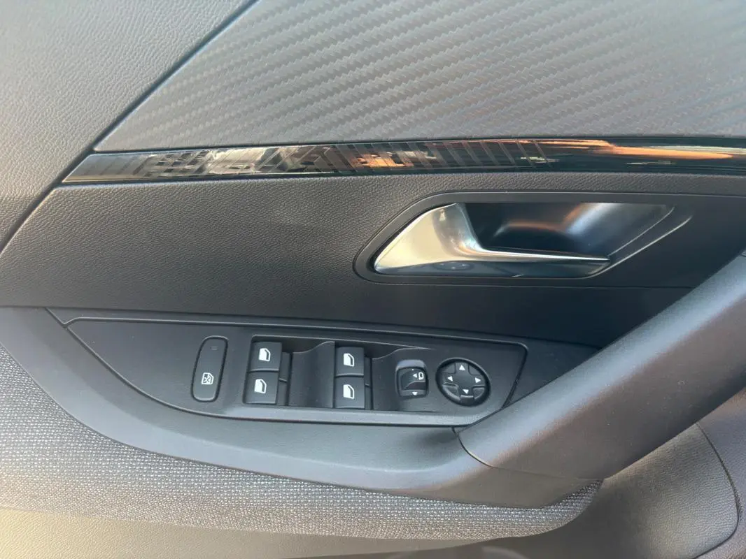 Gros plan sur la commande des vitres et rétroviseurs côté conducteur d’un Peugeot 2008 gris, version Hybrid 145 Style.