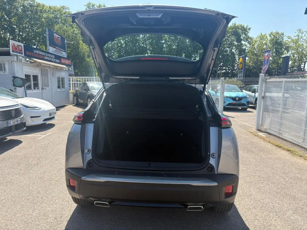 Vue arrière d'un Peugeot 2008 Hybrid 145 gris 2025 avec coffre ouvert et feux arrière allumés en plein jour.
