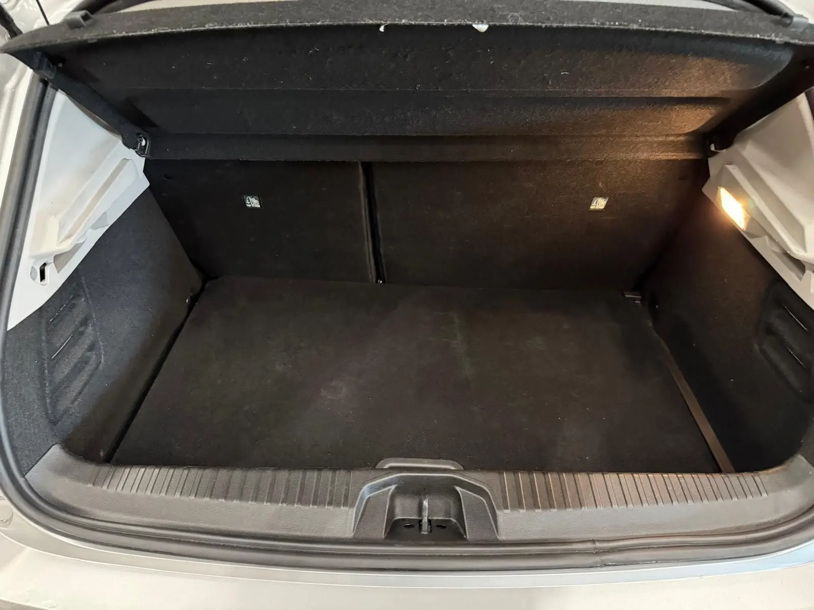 Coffre ouvert vu de l'arrière d'une Renault Clio V gris aluminium, montrant un espace de chargement propre et éclairé.