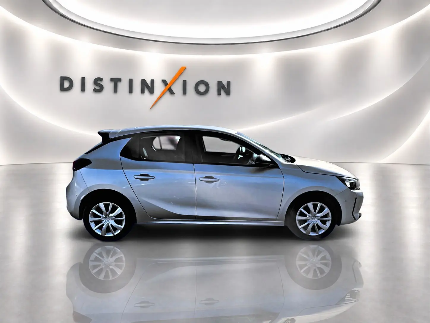 Profil droit d'une Opel Corsa gris alu 2025 dans un showroom lumineux avec reflet au sol et logo Distinxion en arrière-plan.