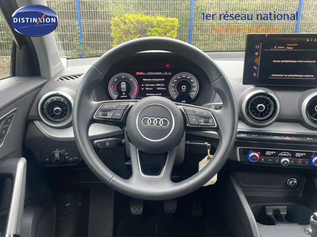 Vue intérieure centrée sur le volant noir de l'Audi Q2 30 TDI S-Line avec tableau de bord numérique et commandes au volant.