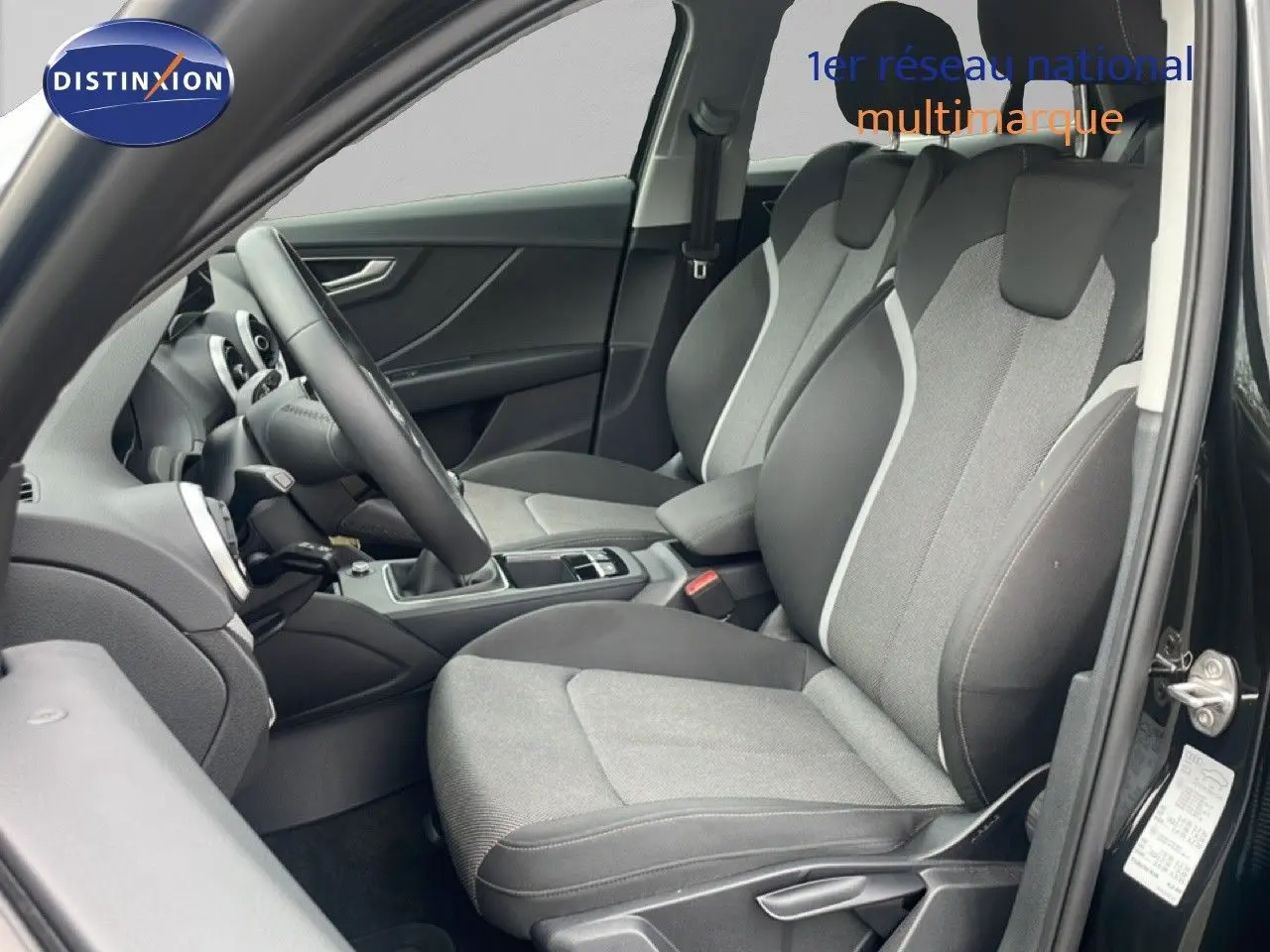 Vue intérieure côté conducteur de l'Audi Q2 30 TDI S-Line 2025, sièges tissu gris et noir, volant cuir multifonction.