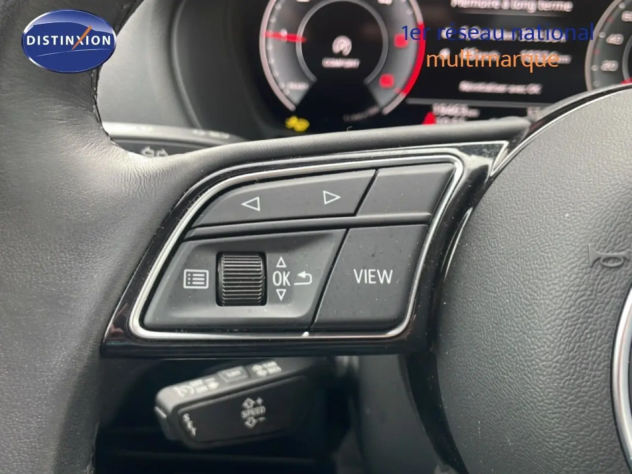 Gros plan sur les commandes au volant côté gauche d’un Audi Q2 noir mito metal, avec tableau de bord numérique en arrière-plan flou.