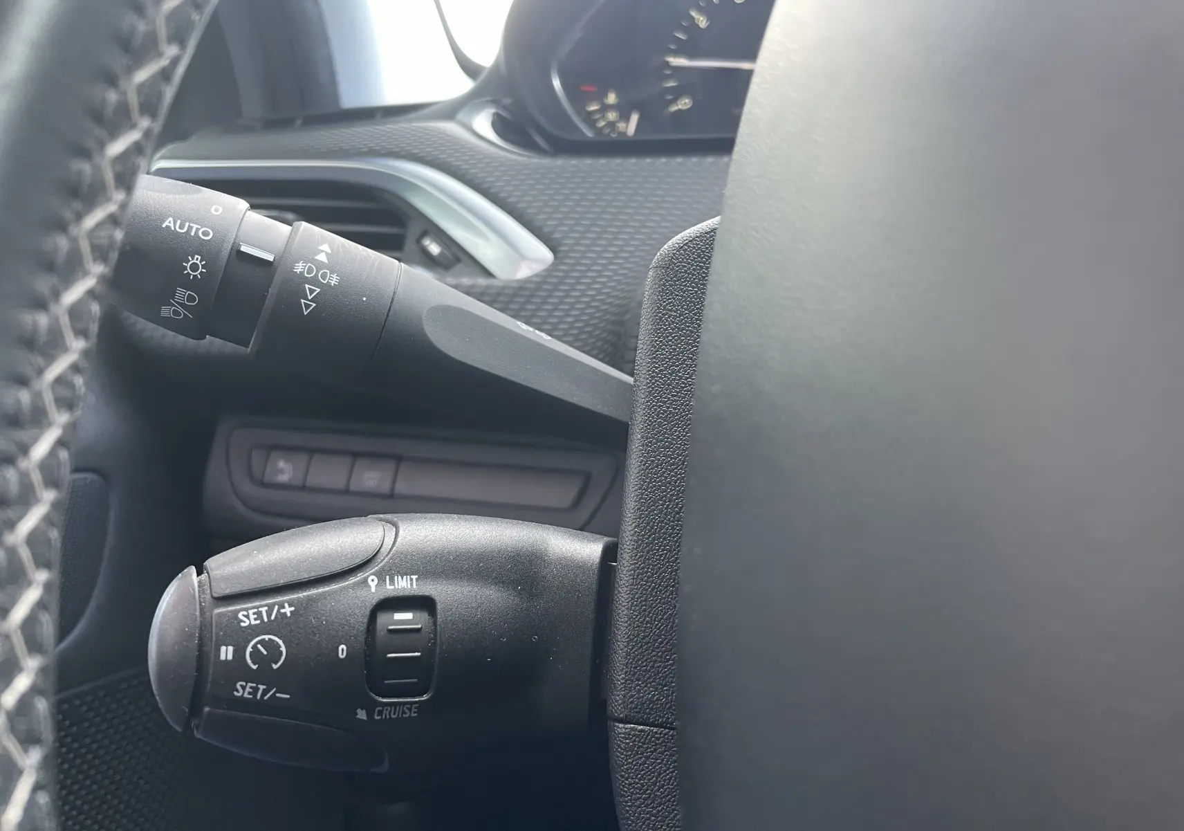 Gros plan sur les commandes de régulateur et des phares à gauche du volant d'un Peugeot 2008 gris, intérieur noir.