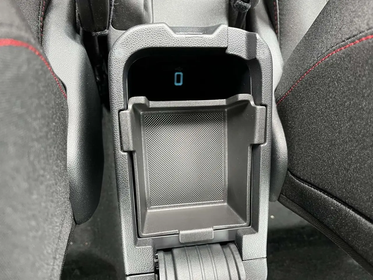 Gros plan sur la console centrale noire du Ford Puma 2023, montrant un rangement ouvert entre les sièges noirs avec surpiqûres rouges.