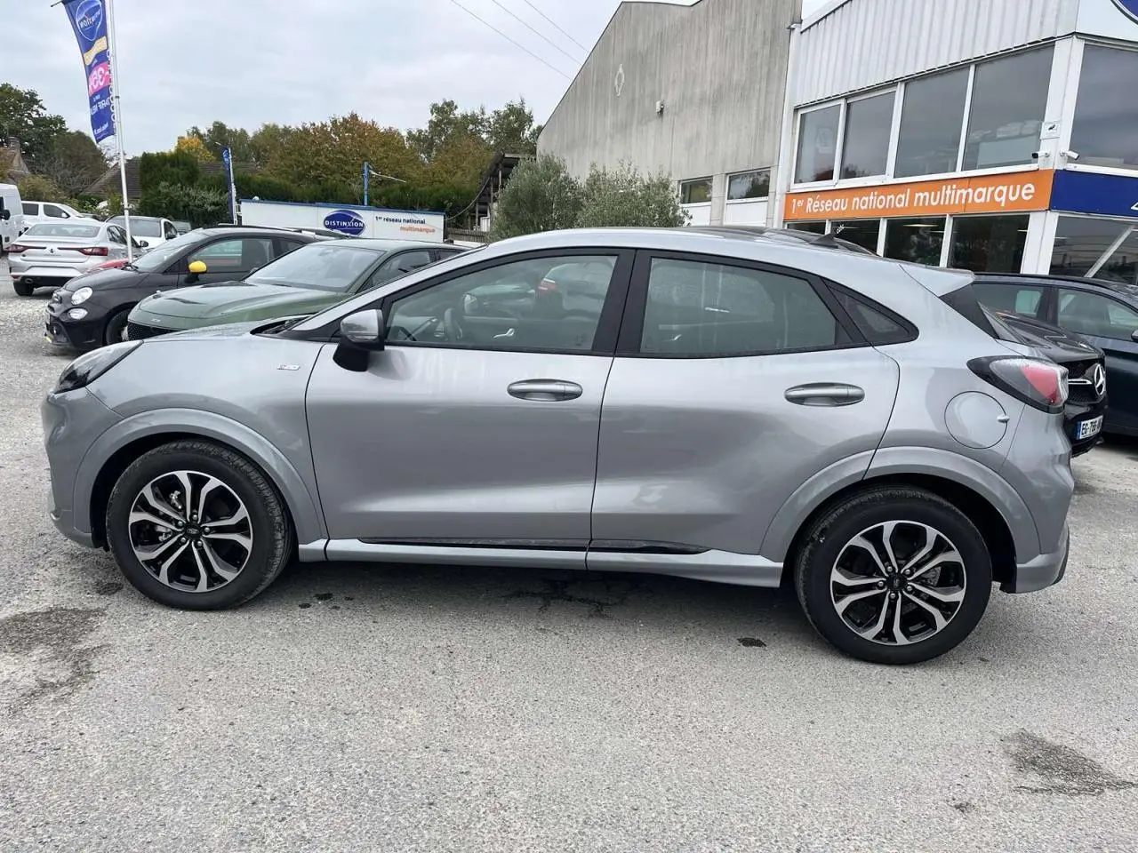 Profil côté gauche du Ford Puma 1.0 EcoBoost mHEV 155 ST Line gris Solar garé en extérieur sur parking.