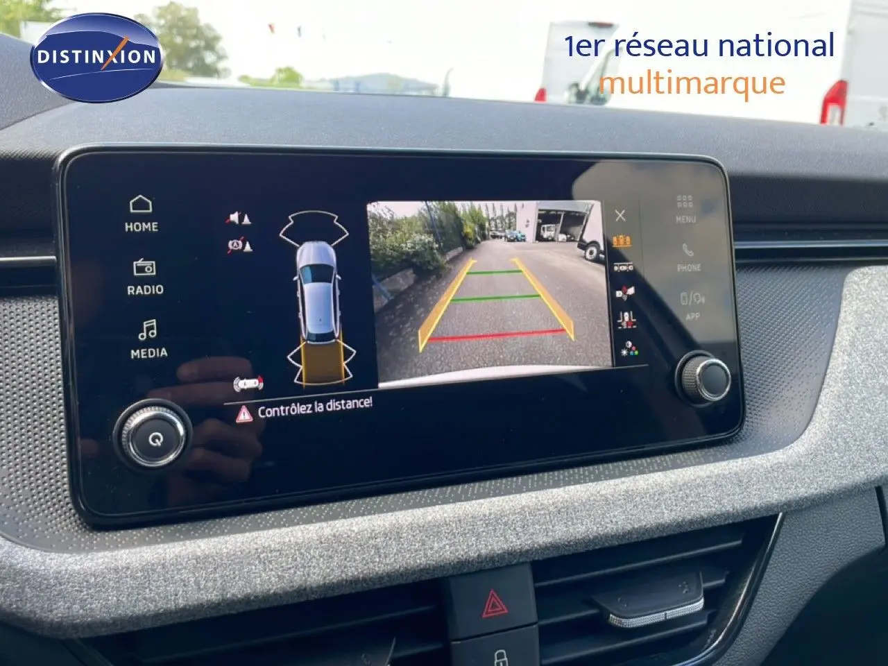 Écran central de la Skoda Scala blanc glacier montrant la caméra de recul avec guidage de trajectoire en extérieur.