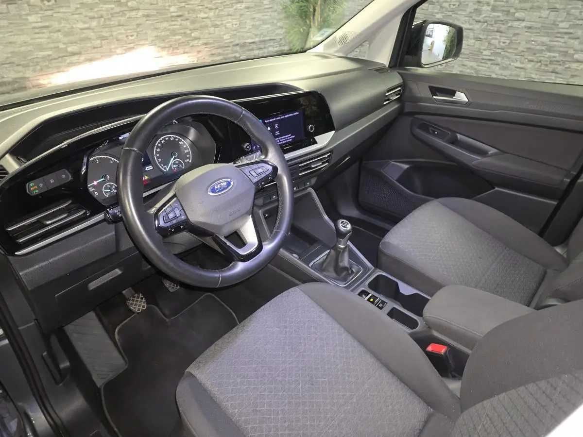 Vue intérieure côté conducteur du Ford Transit Connect gris 2023, volant cuir, boîte manuelle et console centrale moderne.