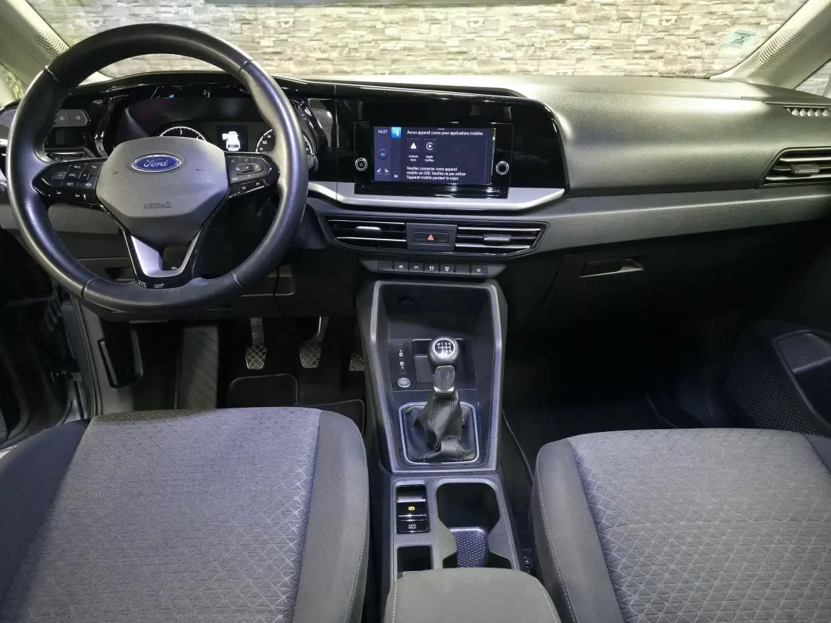 Vue intérieure avant du Ford Transit Connect gris 2023, volant cuir, tableau de bord noir avec écran tactile central.