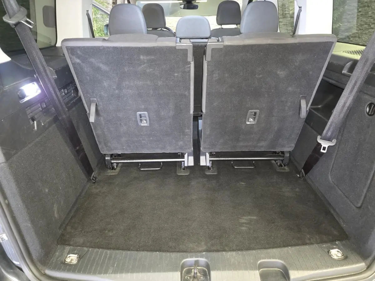 Vue arrière du coffre du Ford Transit Connect gris 2023 avec sièges arrière rabattus et tapis noir.
