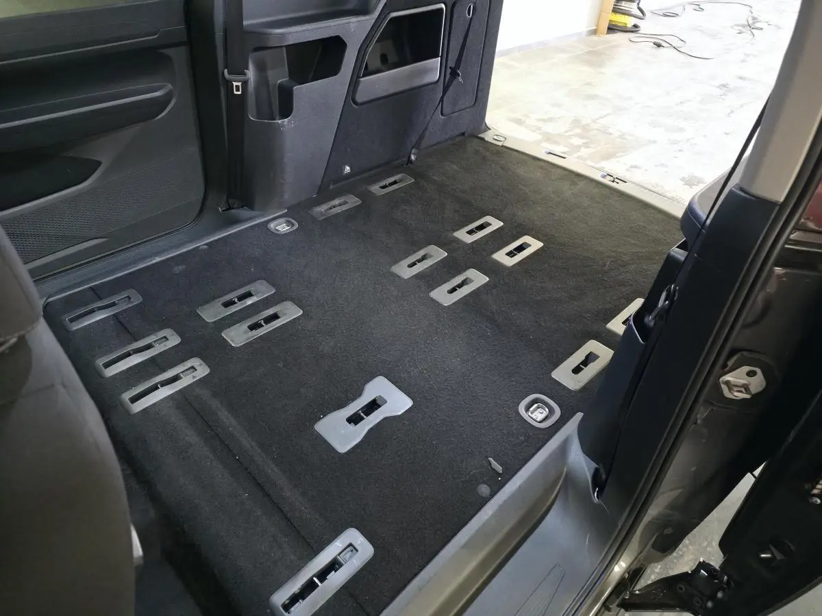 Vue intérieure arrière côté droit du Ford Transit Connect gris, montrant le plancher avec fixations de sièges et porte coulissante ouverte.