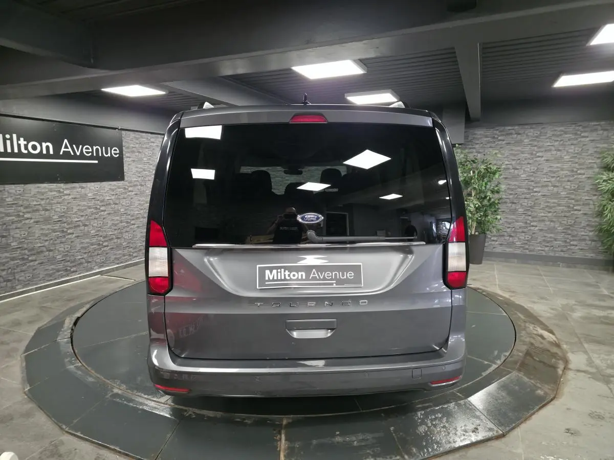 Vue arrière d'un Ford Tourneo Connect gris métallisé dans un showroom avec hayon vitré et feux rouges verticaux.