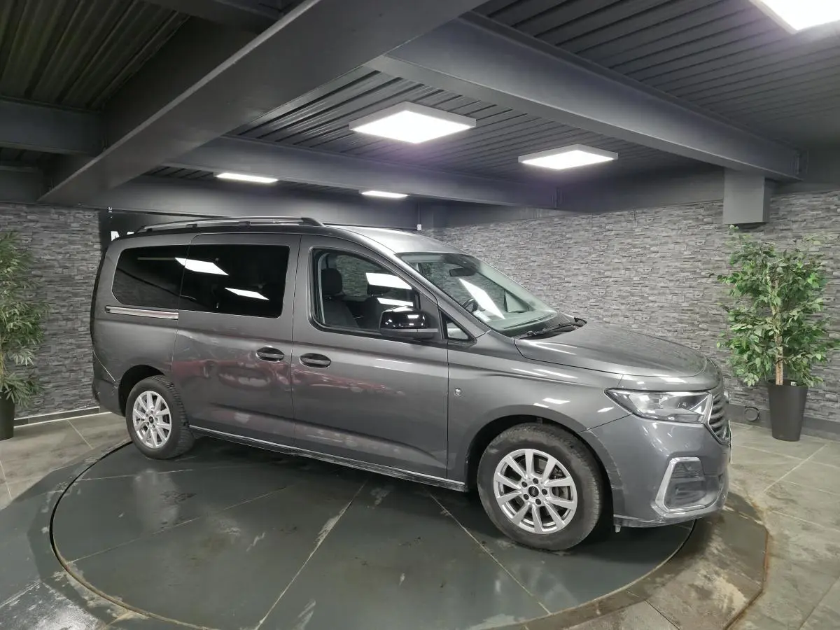 Vue 3/4 avant droit du Ford Transit Connect Tourneo gris métallisé, avec barres de toit argentées et vitres arrière surteintées.