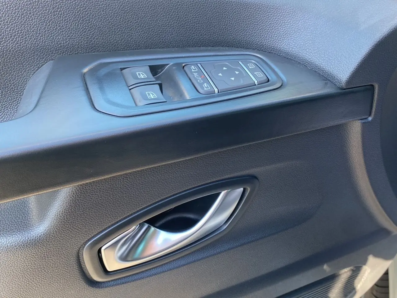 Poignée intérieure et commandes électriques de la porte avant gauche du Renault Trafic Combi gris Highland 2025.