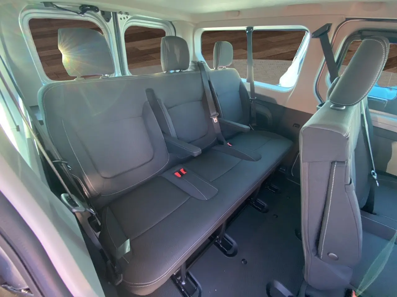 Vue intérieure arrière du Renault Trafic Combi 2025 gris Highland, sièges tissu noir avec ceintures et accoudoirs visibles.