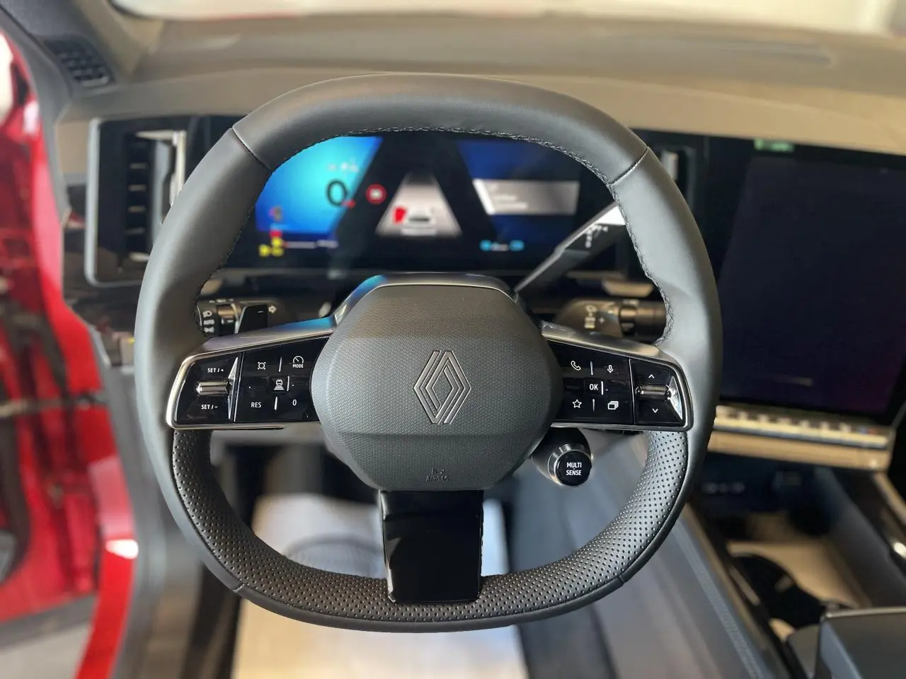 Volant en textile refined noir avec commandes intégrées et logo Renault, intérieur du Renault Rafale rouge visible côté conducteur.