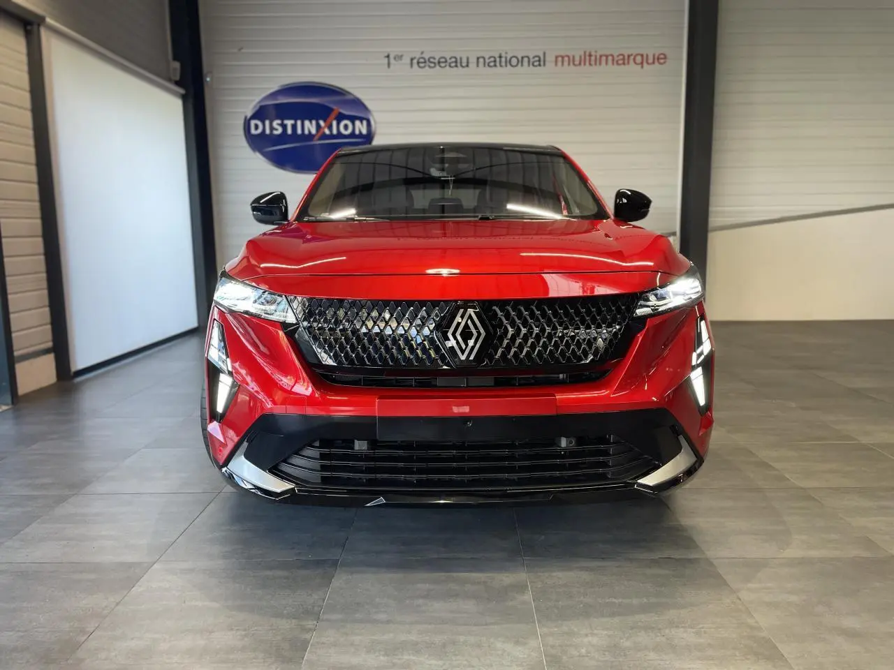 Vue frontale d'un Renault Rafale 2025 rouge à toit noir avec calandre noire et feux LED distinctifs en intérieur showroom.