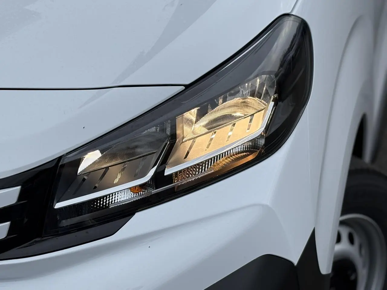 Gros plan sur le phare avant droit du Peugeot Expert Fourgon blanc Icy, avec partie de la roue et pare-chocs noir visible.