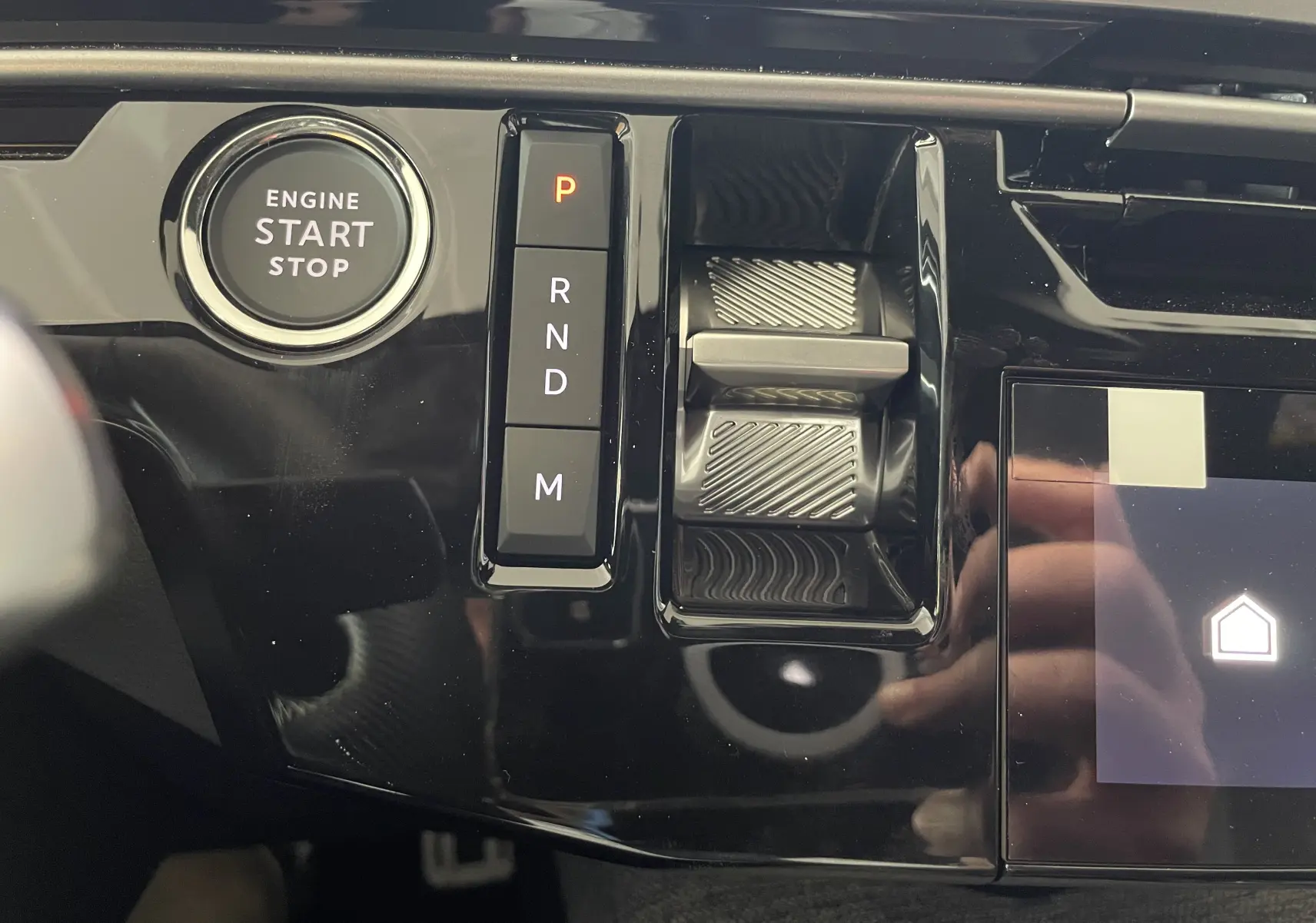 Gros plan sur la console centrale noire brillante du Peugeot 3008 Hybrid avec bouton start/stop et commandes de boîte automatique.