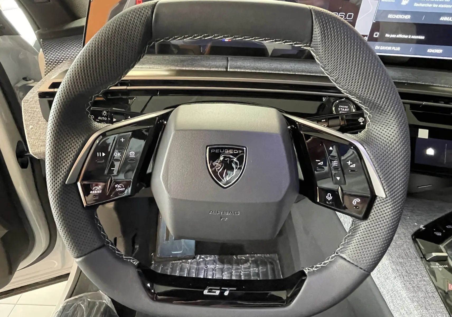 Vue rapprochée du volant GT noir perforé avec logo Peugeot au centre dans l'habitacle du 3008 Hybrid blanc.