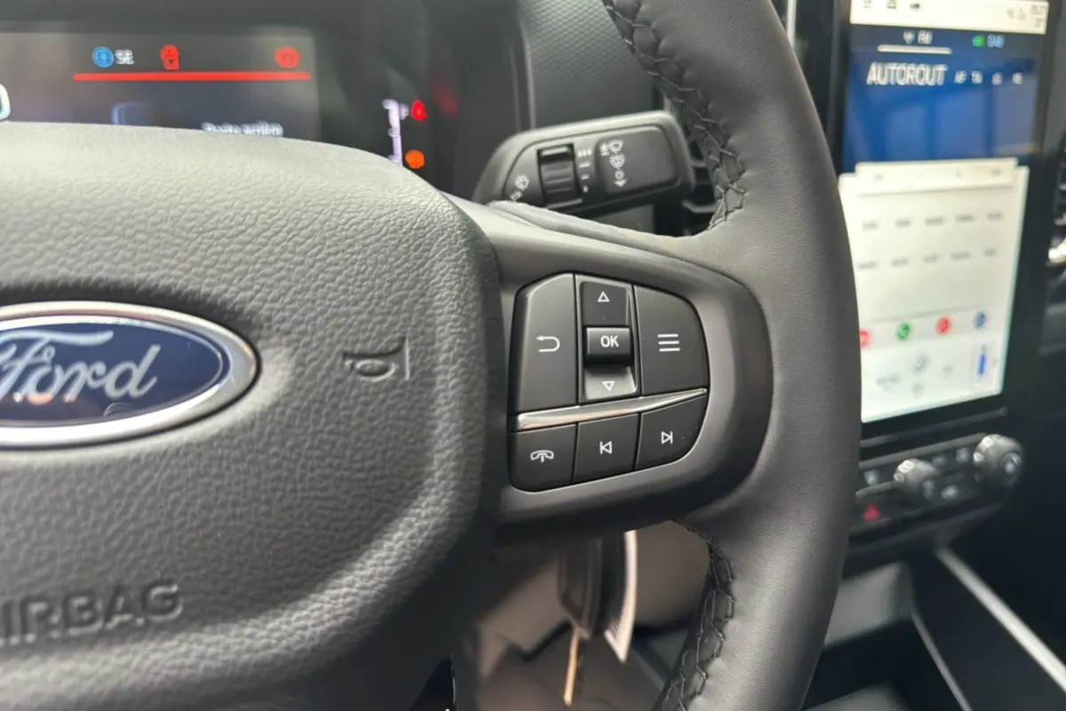 Gros plan sur le volant cuir multifonctions Ford Ranger 2025 avec commandes intégrées et écran tactile en arrière-plan.