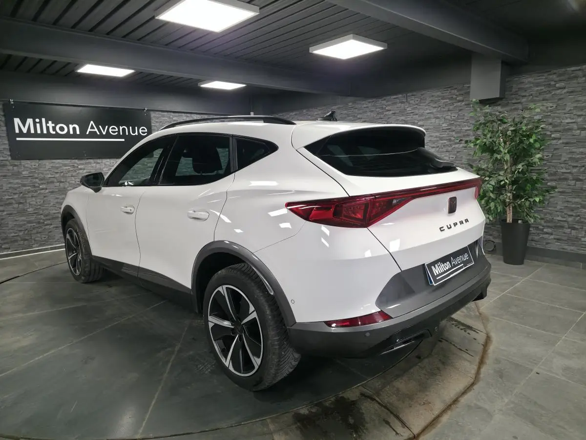 Vue 3/4 arrière droite du CUPRA Formentor blanc avec jantes alliage noires et bandeau lumineux arrière LED dans un showroom.