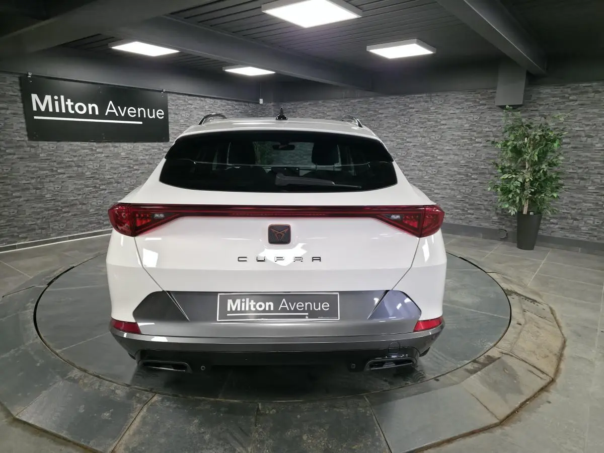 Vue arrière d'un CUPRA Formentor blanc avec bandeau lumineux rouge et double sortie d'échappement noire en intérieur showroom.
