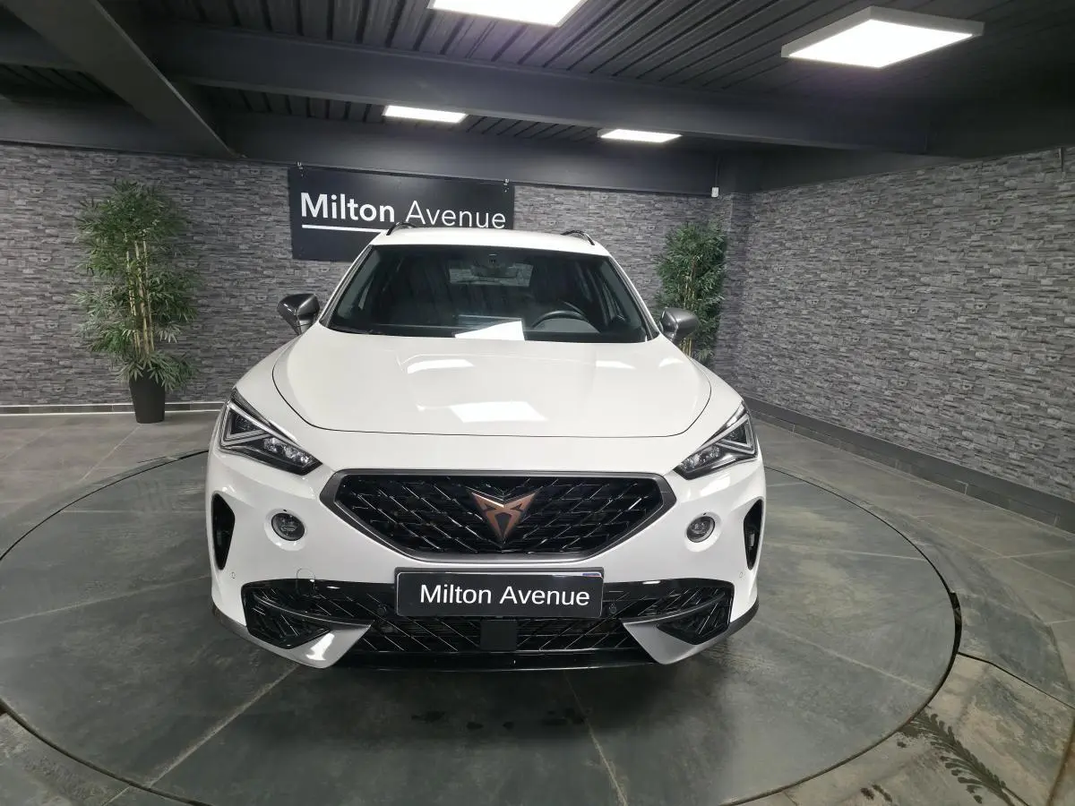 Vue avant d'une CUPRA Formentor blanche 2024 avec calandre noire et logo cuivre, dans un showroom au sol circulaire.