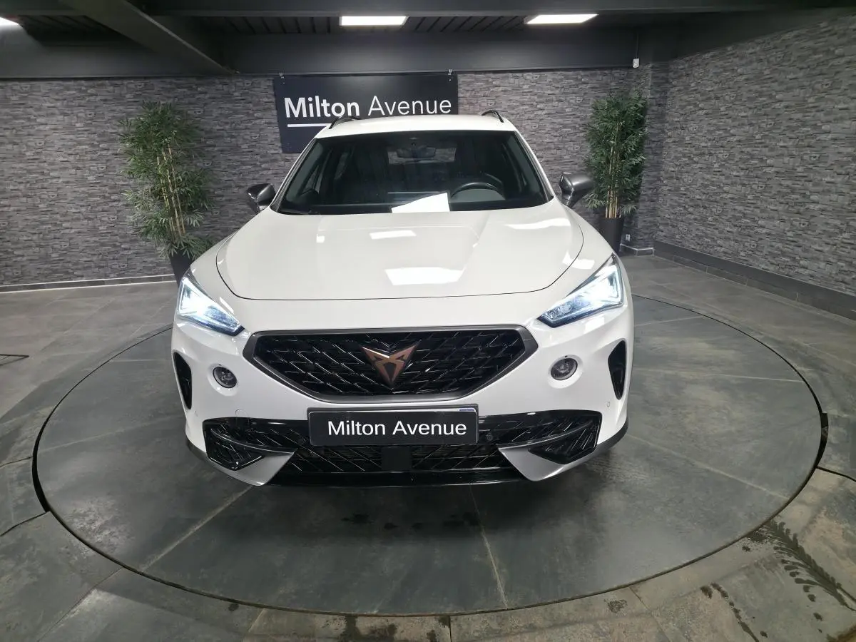 Vue frontale du CUPRA Formentor blanc avec calandre noire et feux LED allumés dans un showroom.