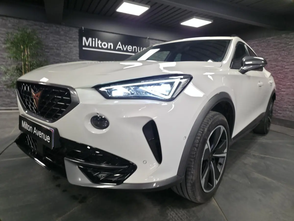 Vue 3/4 avant droit d'une CUPRA Formentor blanche avec calandre noire et phares LED allumés dans un showroom.