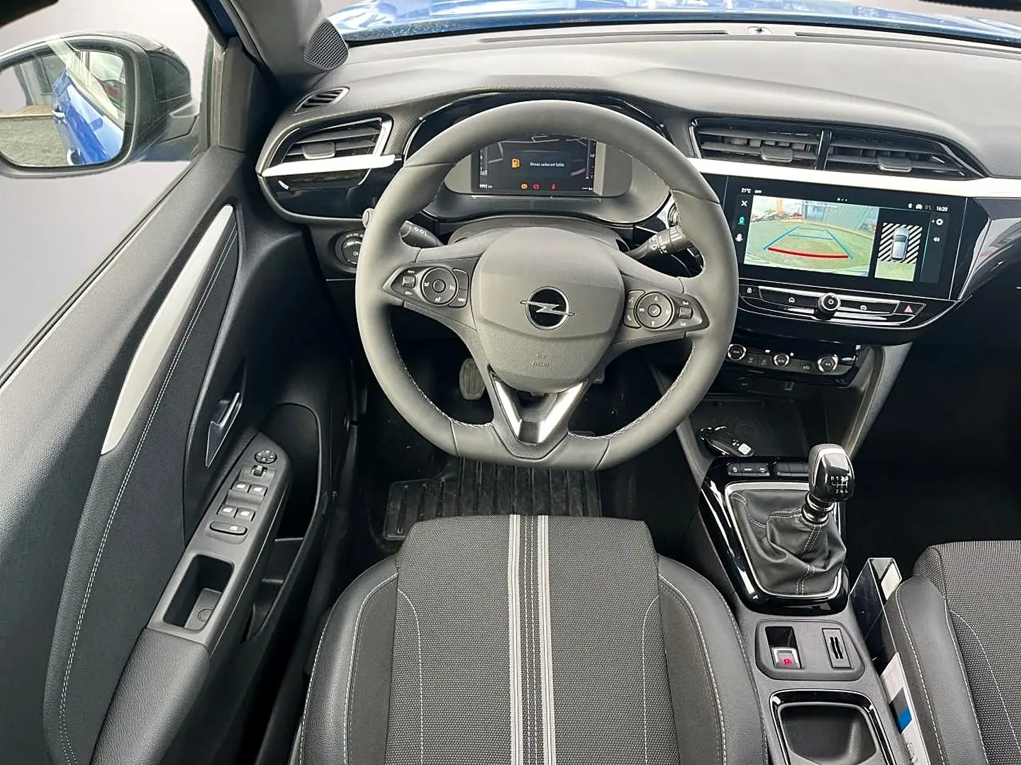 Vue intérieure avant centrée sur le volant sport et la console avec écran tactile, sièges noirs à surpiqûres grises.