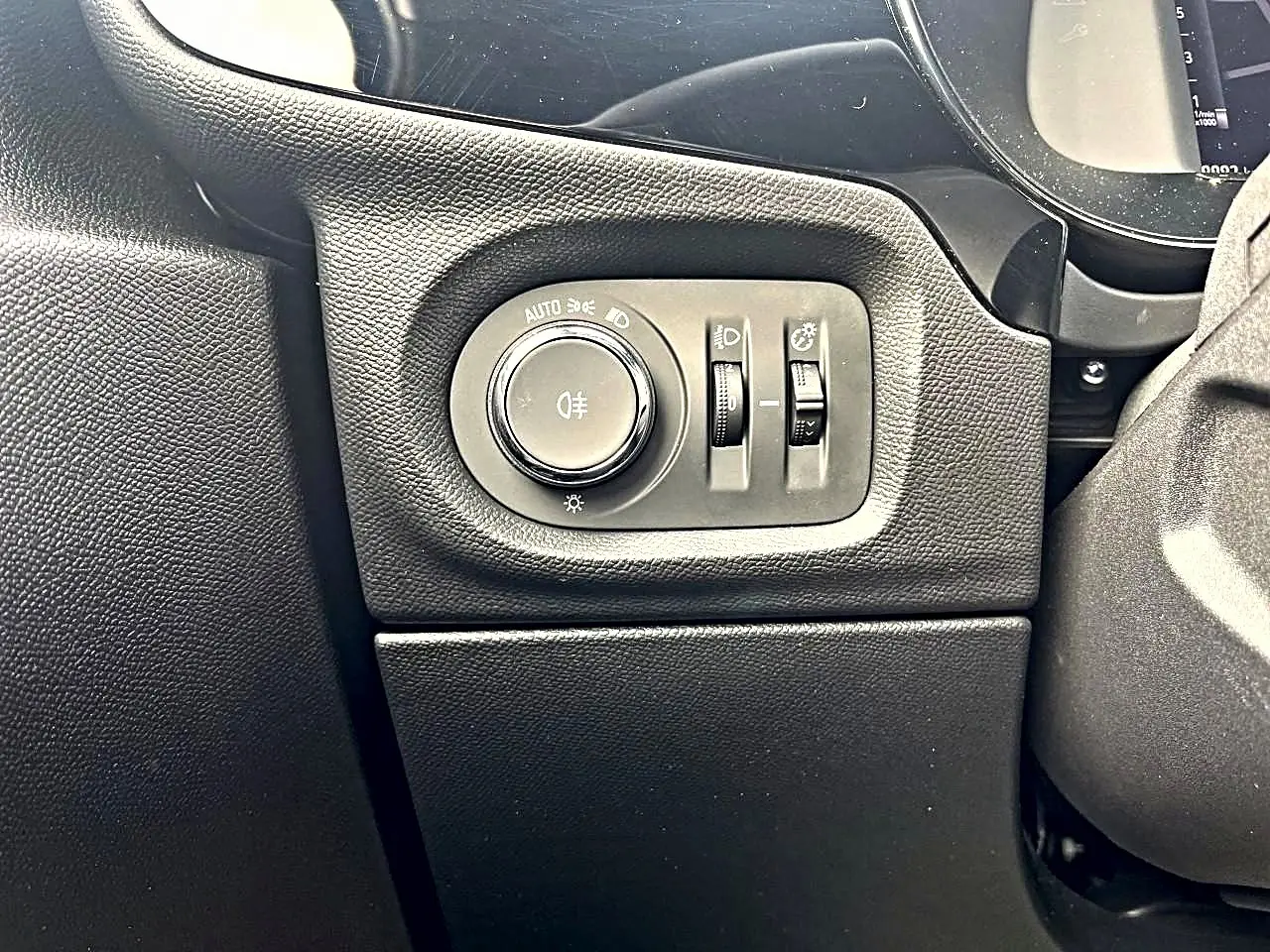 Gros plan sur les commandes d’éclairage noires à gauche du volant dans l’habitacle de l’Opel Corsa bleu 2025.