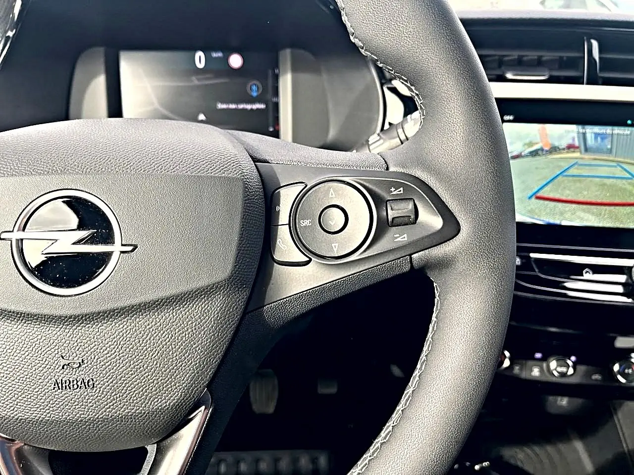 Gros plan sur le volant sport noir de l’Opel Corsa 2025 avec commandes multifonctions et écran tactile de caméra de recul.