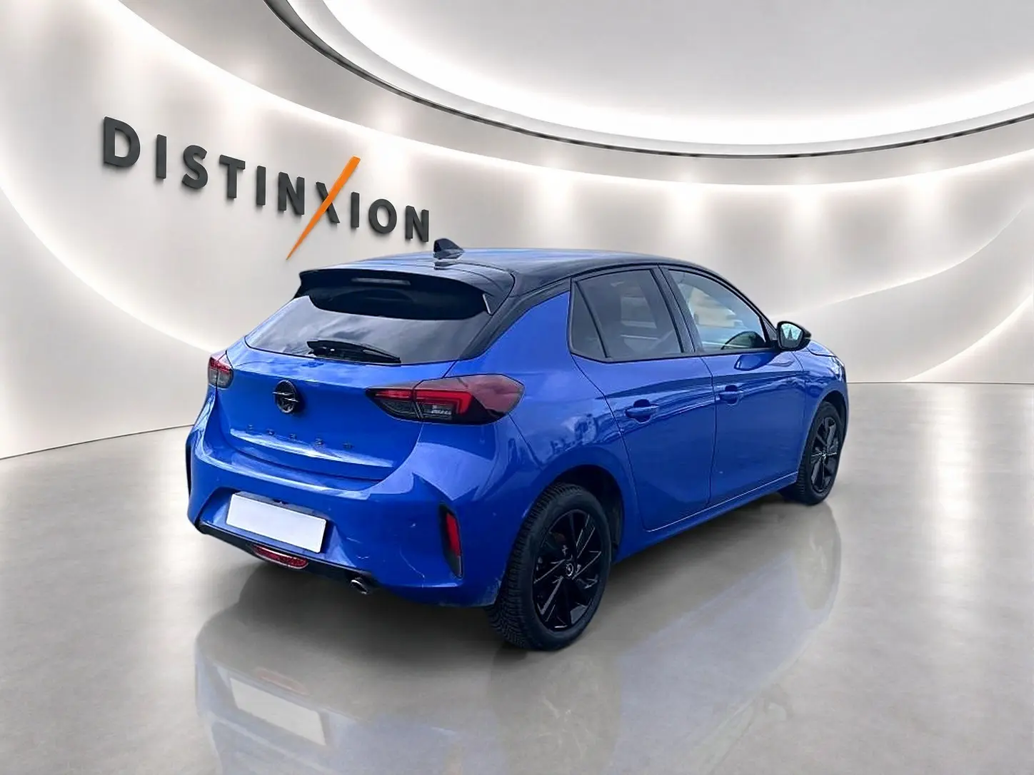 Vue 3/4 arrière droite d'une Opel Corsa 1.2 turbo bleu avec jantes noires et becquet arrière dans un showroom.