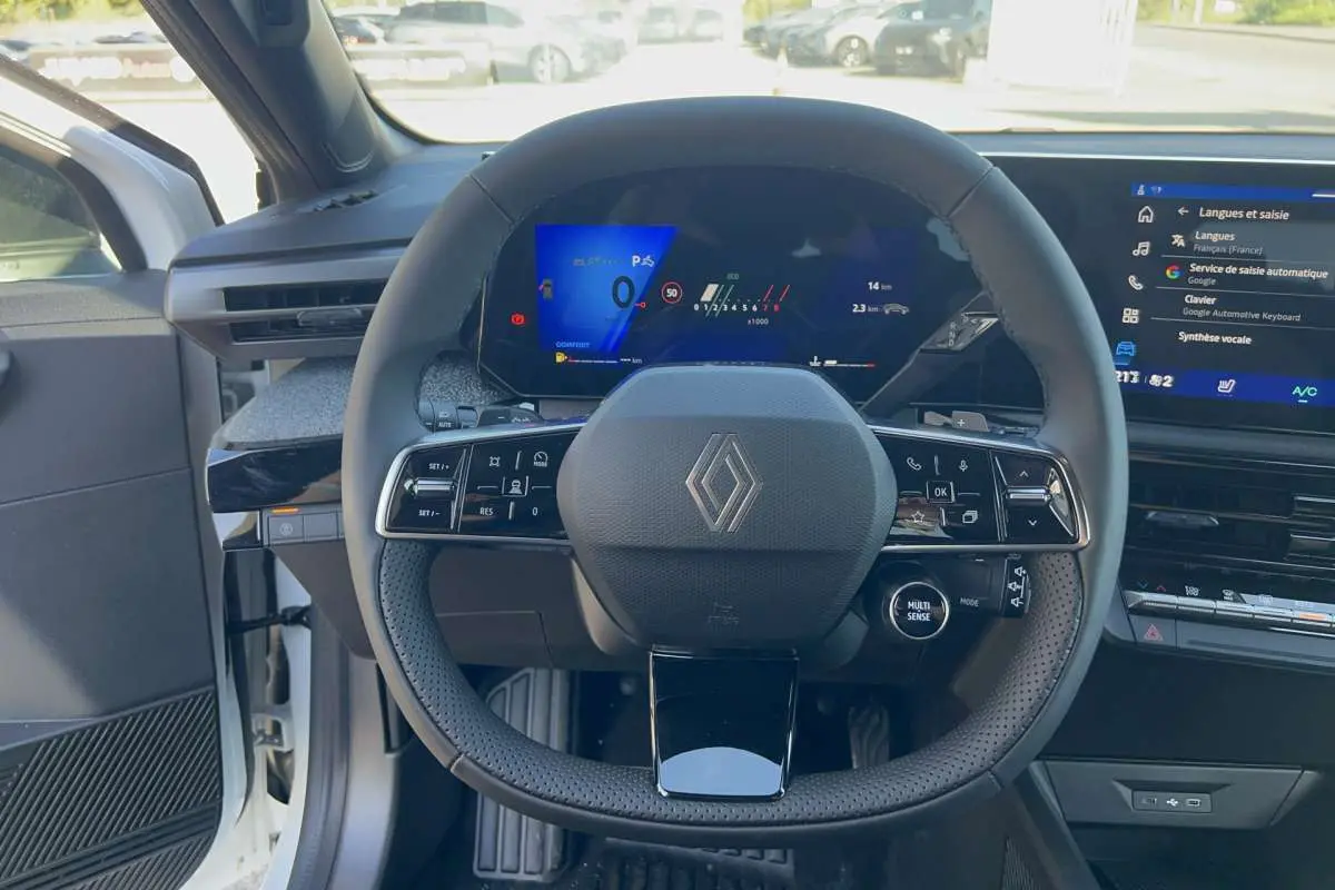 Vue intérieure centrée sur le volant multifonctions de la Renault Clio blanc glacier avec tableau de bord numérique et écran tactile.