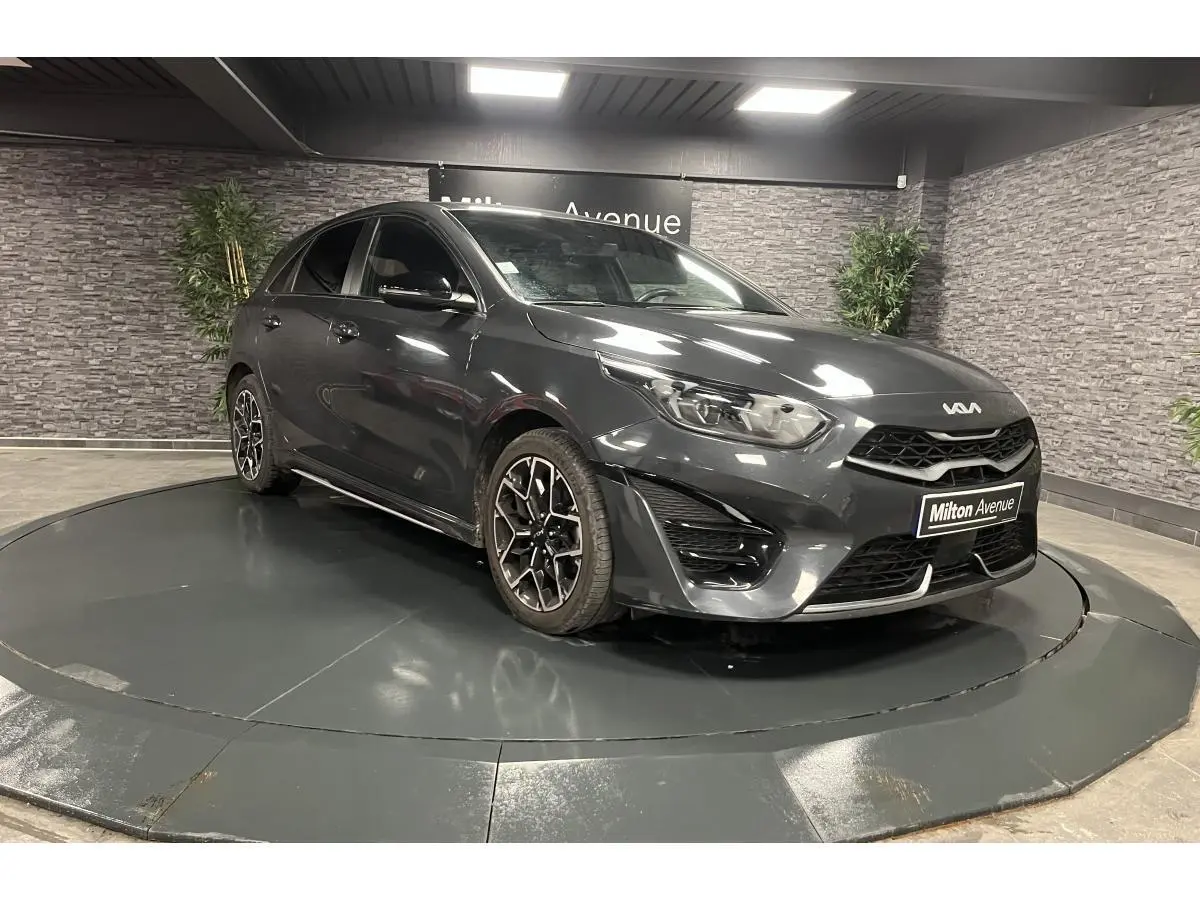Kia Ceed gris métallisé vue 3/4 avant droit avec jantes alliage et calandre noire laquée dans showroom.