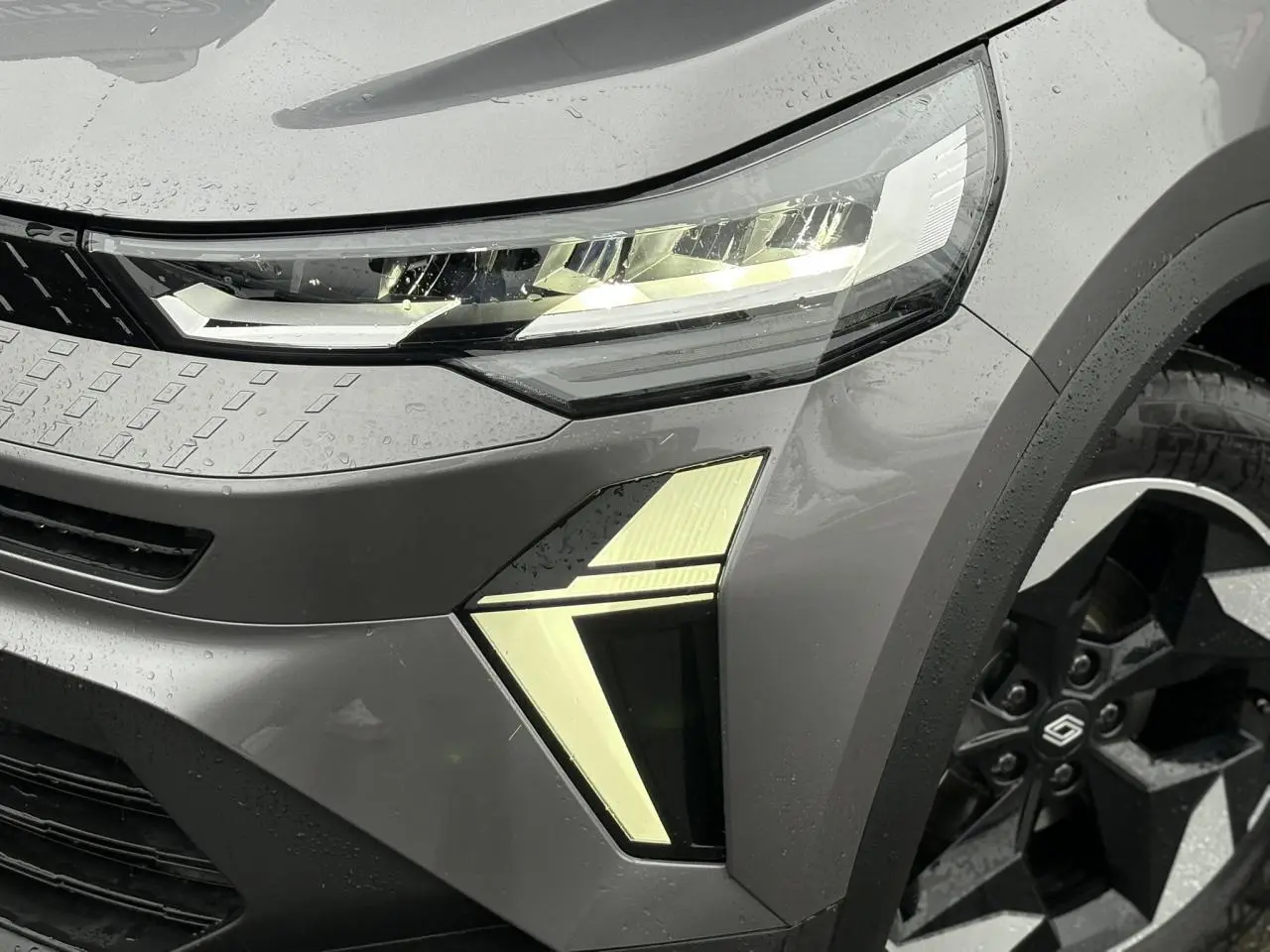 Gros plan sur l'avant droit gris Cassiopée du Renault Captur 2025, mettant en valeur le phare LED et la jante noire distinctive.