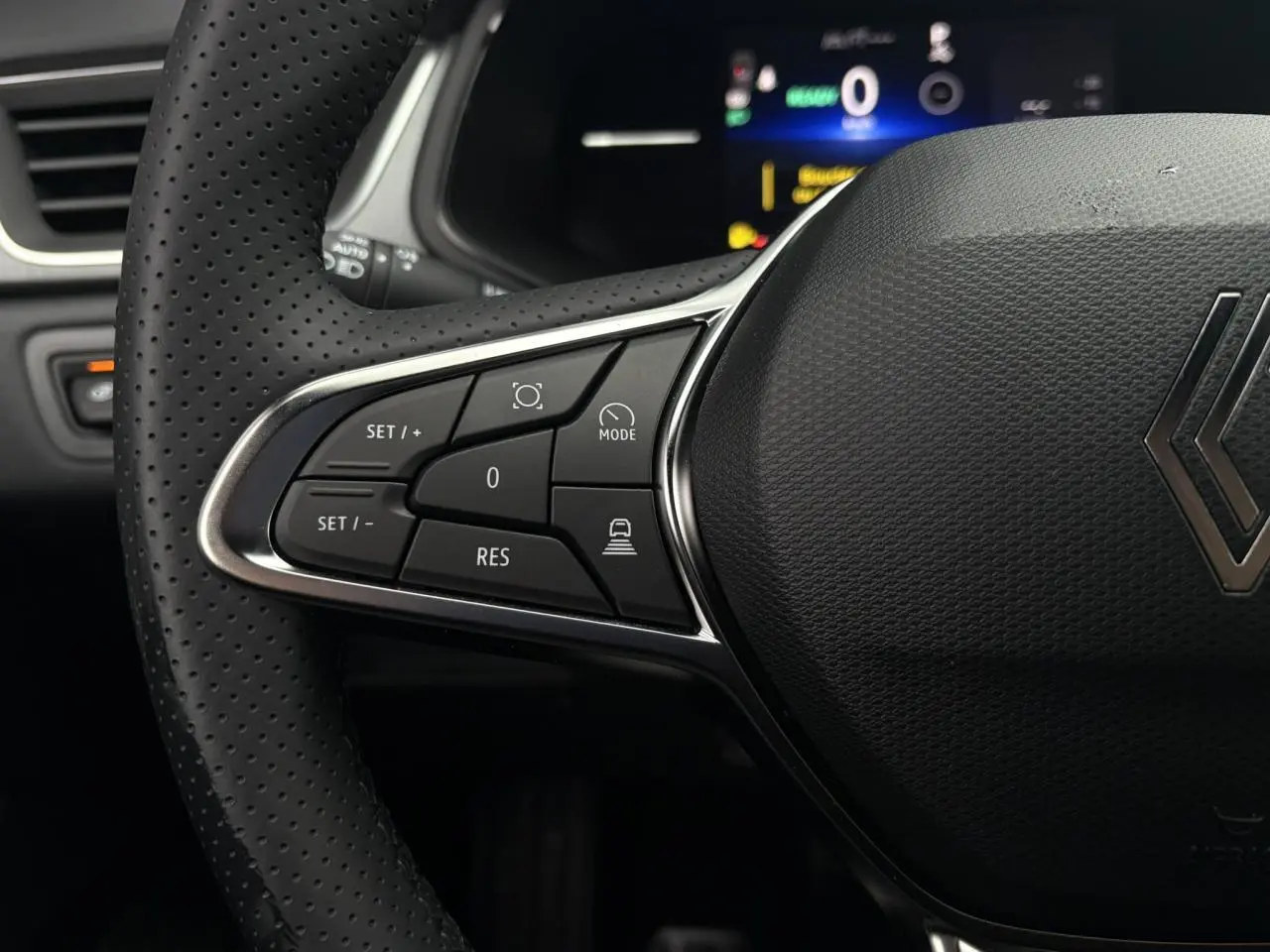 Gros plan sur le volant perforé noir du Renault Captur 2025 avec commandes de régulateur adaptatif et écran numérique en arrière-plan.