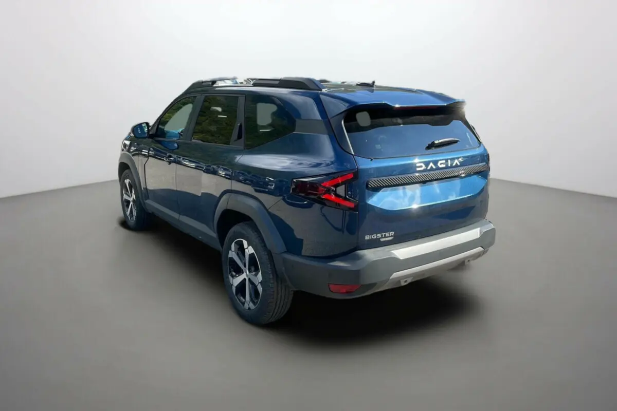 Vue 3/4 arrière droite du Dacia Bigster Hybrid 155 Journey City bleu indigo avec barres de toit et jantes alu 18 pouces.