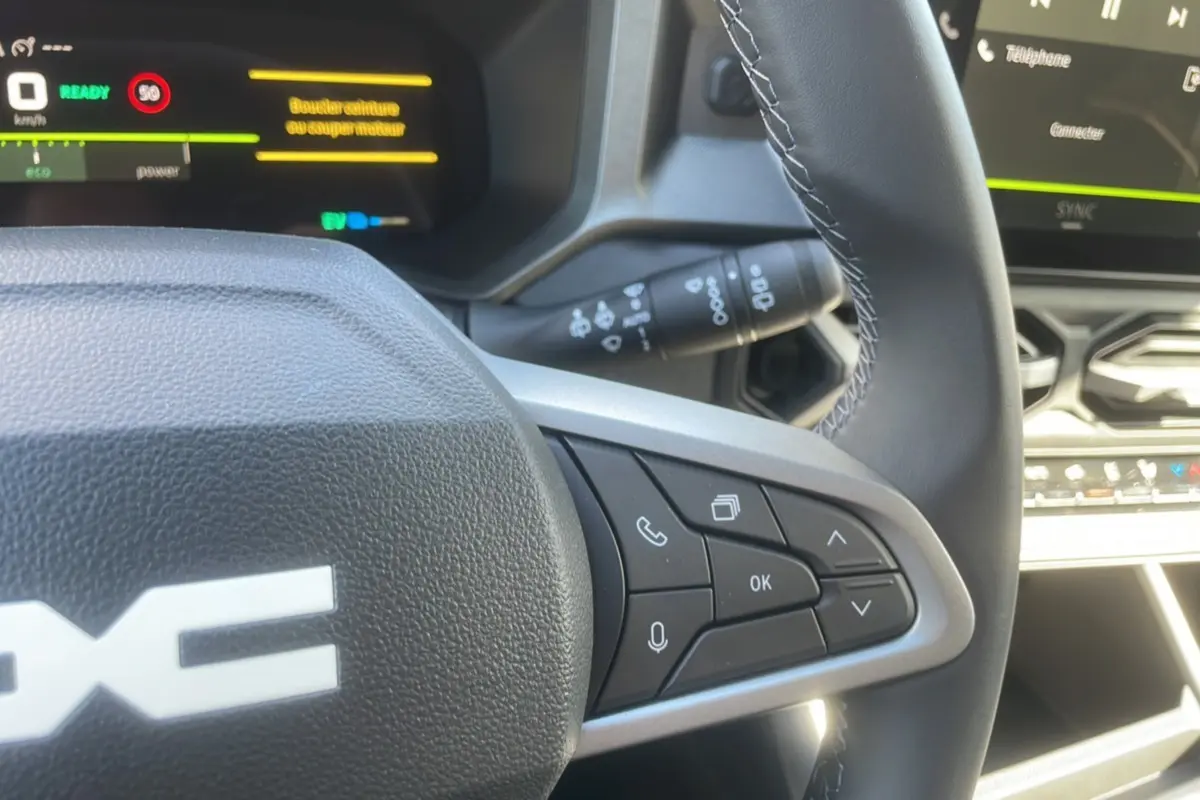 Gros plan sur le volant cuir de la Dacia Bigster Hybrid 155, avec commandes multifonctions et tableau de bord digital.
