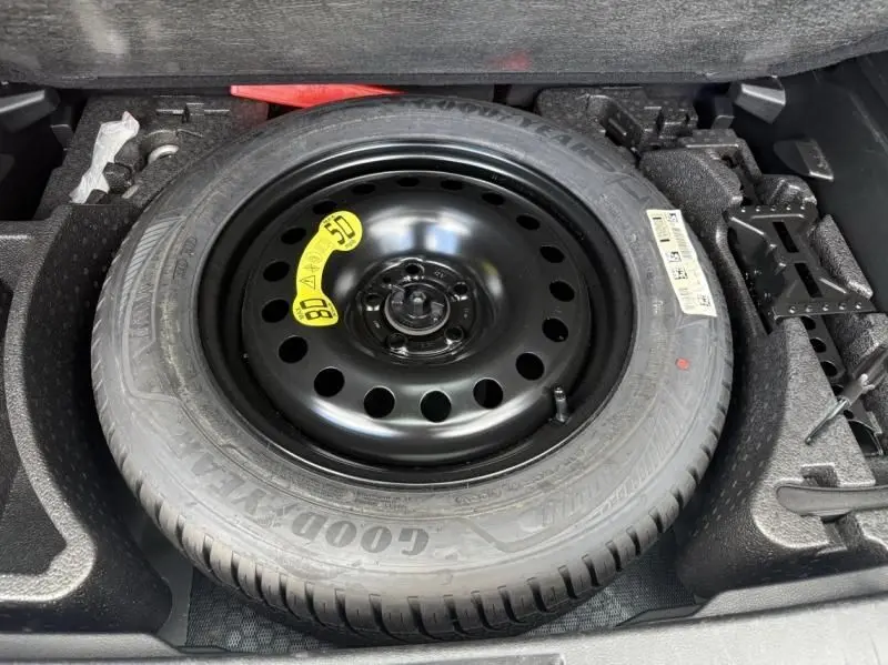 Roue de secours noire Goodyear dans le coffre d’un Jeep Renegade 2024 bleu métal, vue en plongée sur le pneu et son emplacement.