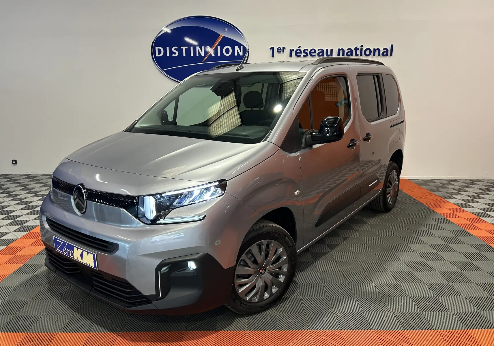 Citroën Berlingo Multispace gris acier en 3/4 avant droit, avec barres de toit noir brillant et phares LED allumés.