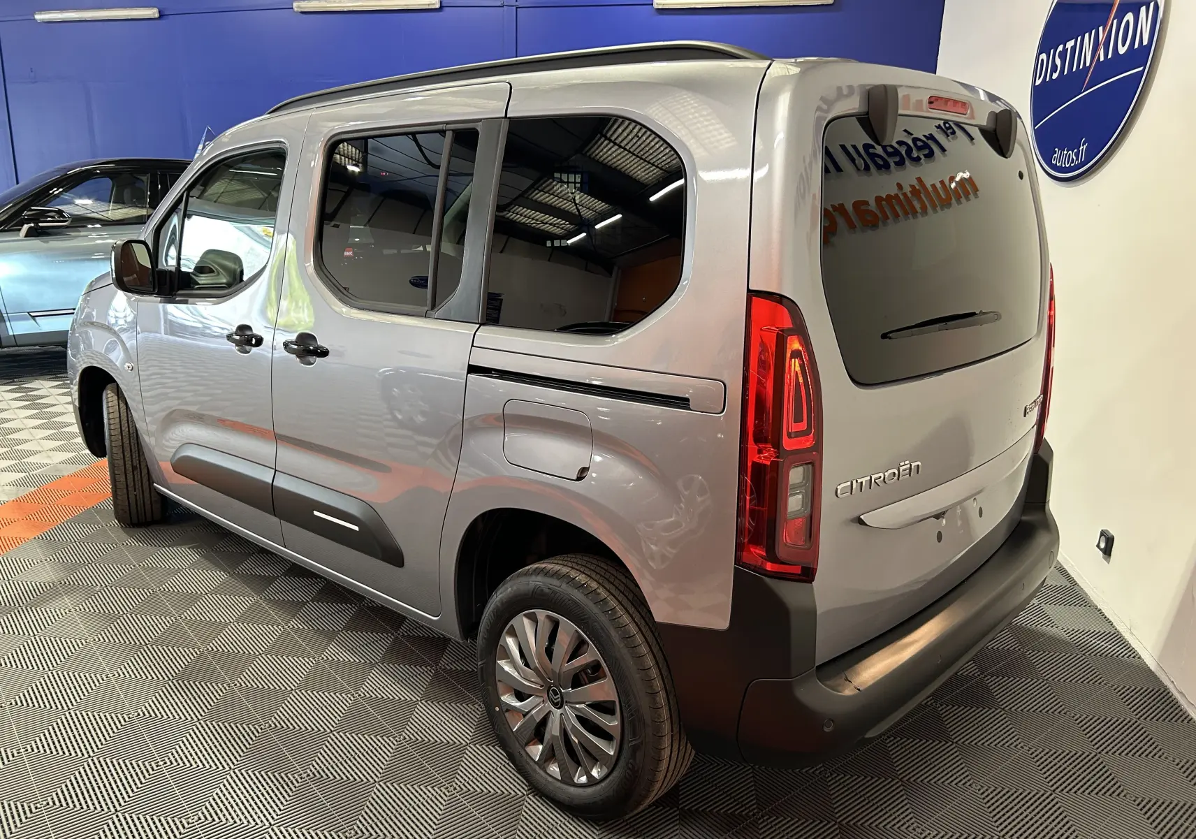 Vue 3/4 arrière droite du Citroën Berlingo Multispace gris acier avec vitres surteintées et barres de toit noir brillant.